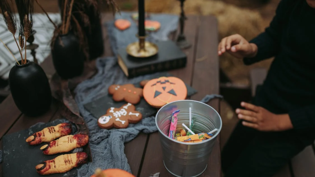 Halloween party activities to keep guests entertained l Free A Person Sitting at a Table with Halloween Decorations and a Bucket of Candies Stock Photo